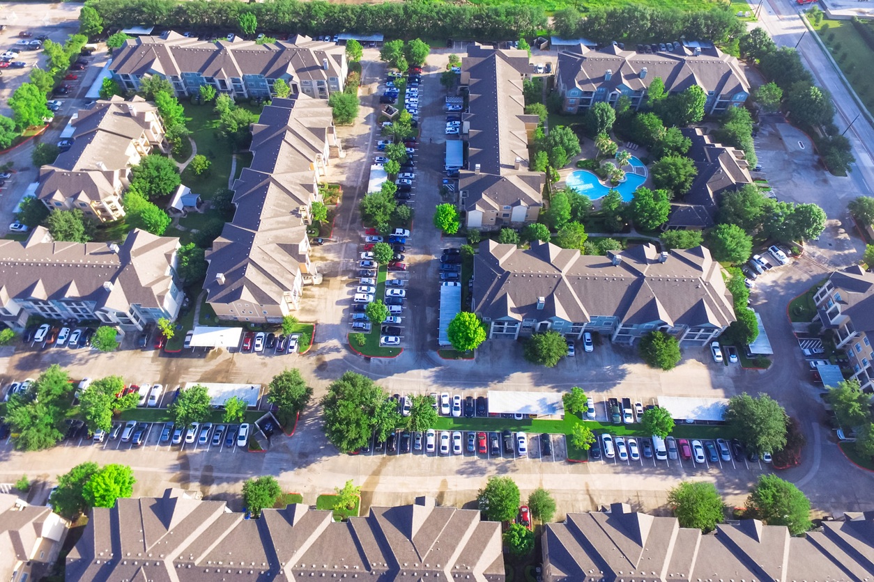 Aerial View Of Typical Multi Level Apartment Building With Swimming Pool, Surrounded By Green Garden And Rows Of Cars In Parking Lots In Houston, Texas, Us. Apartment Complex Next To Road With Traffic