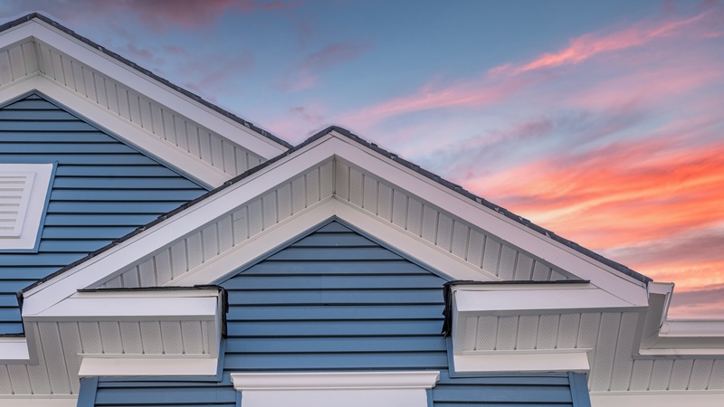 Triangle Shape Decorative Gable With Colonial White Soffit And Fascia On A Blue Horizontal Vinyl Siding Modern American Estate Home With Colorful Dramatic Stunning Orange Sunset Sky