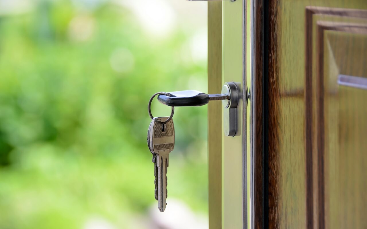 A close up of a front door that's opened with a key in a lock hanging from it.