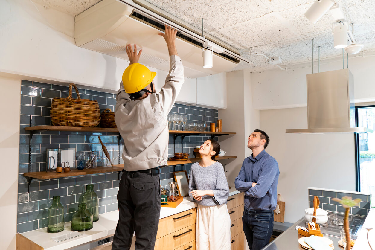 Home inspector on a ladder checking indoor ventilation in a couple's kitchen