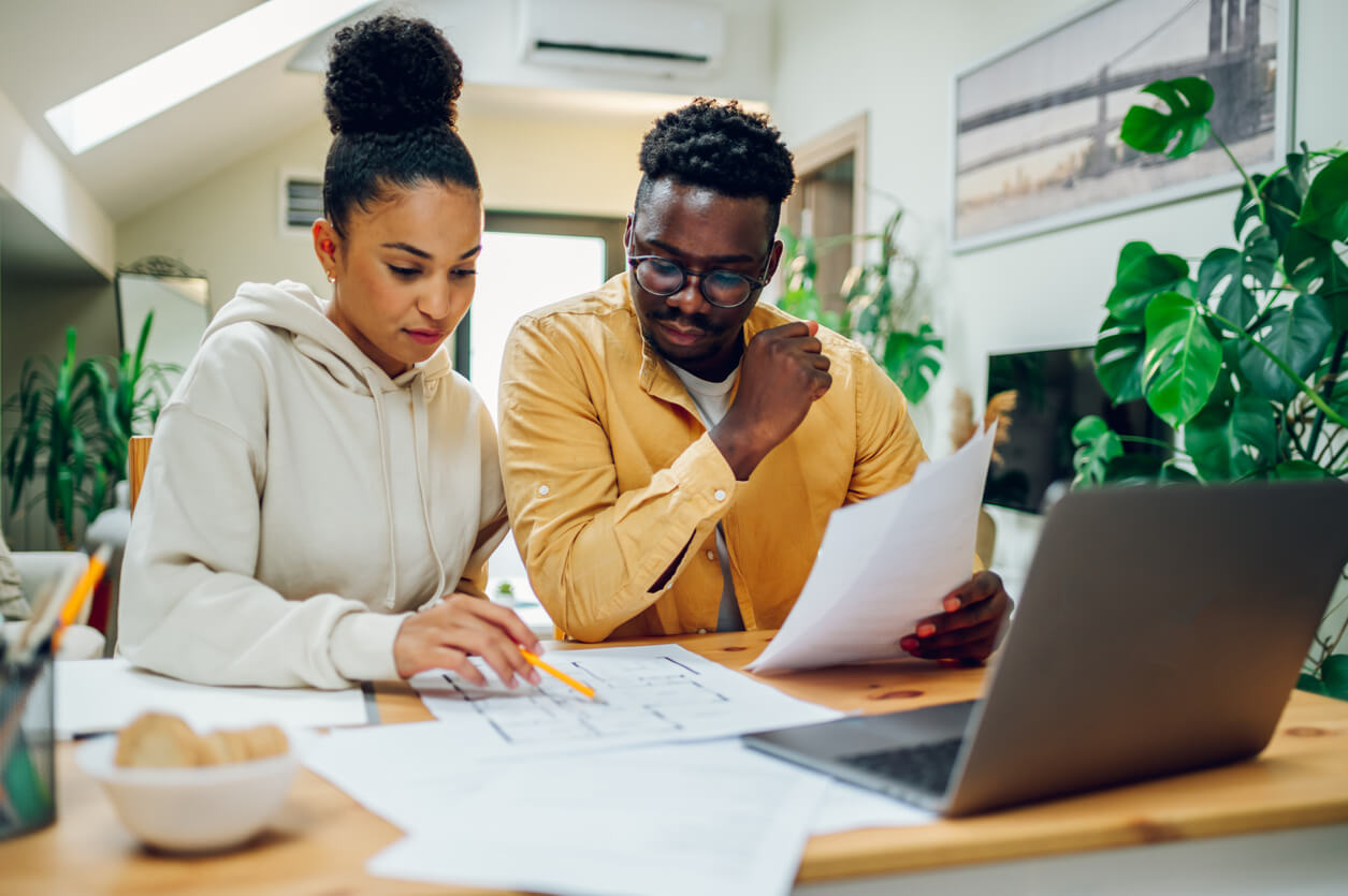 a Black couple reviewing paperwork in front of a laptop and discussing home improvement plans
