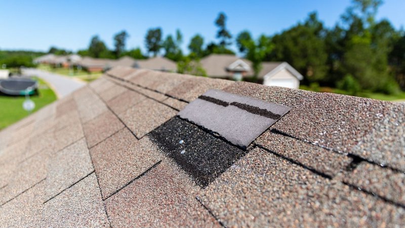 A close-up of damaged shingles revealing the underlayment, illustrating Signs You Need a New Roof.
