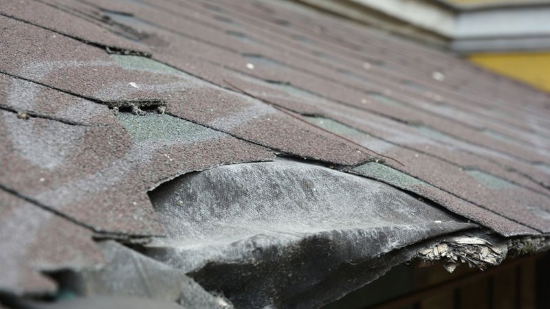 A close-up of torn and missing asphalt shingles, showing clear Signs You Need a New Roof.